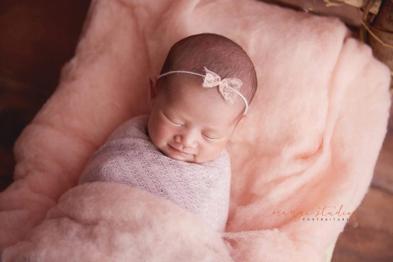15 days old smiling baby girl on log bed newborn portraits in singapore studio