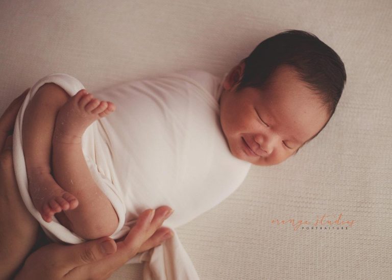 13 days old smiling baby boy newborn portraits in mum's hands in singapore studio