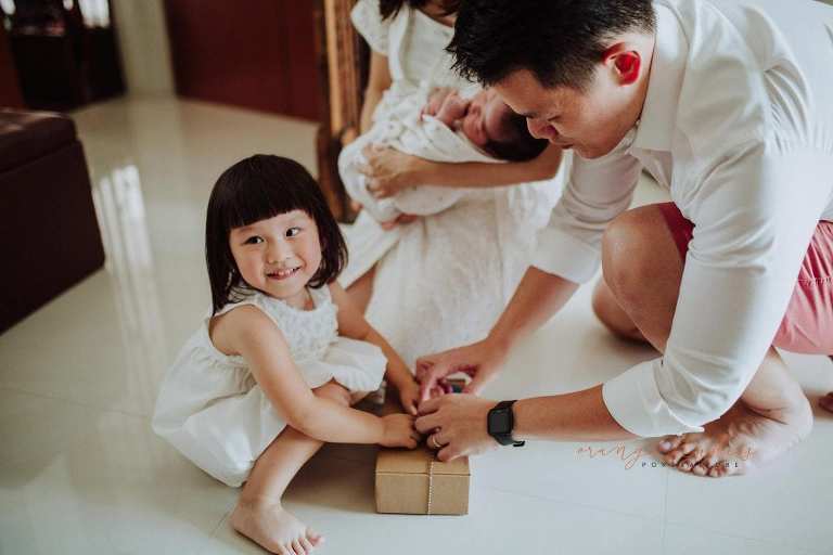 elder sister unwrapping gift from younger sister during fresh 48 photoshoot at home