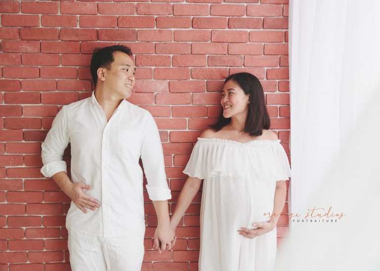 maternity portraits with husband against brick wall in singapore studio with natural light