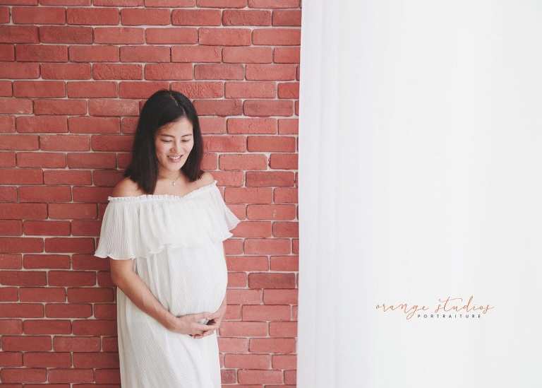 maternity portraits against brick wall in singapore studio with natural light