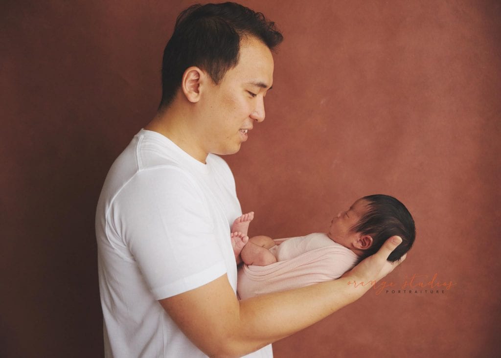 dad smiling and looking at newborn baby girl in singapore home natural lighting