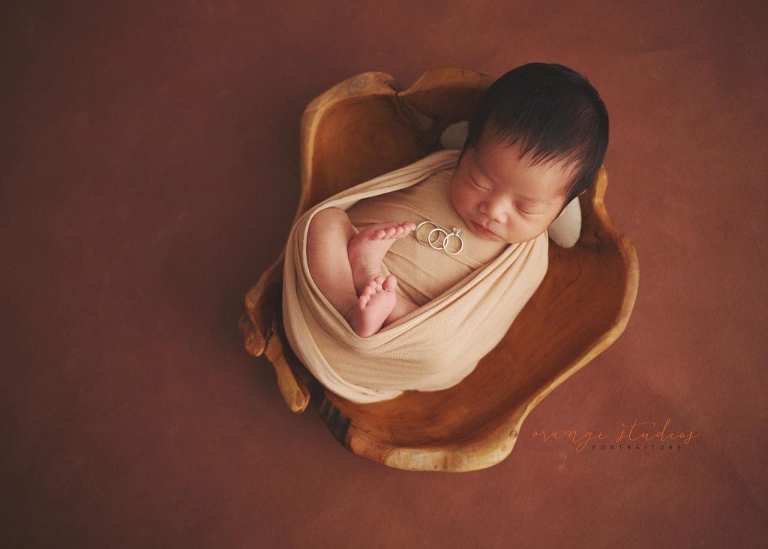 newborn baby in wooden bowl prop with parents' wedding bands and rings in singapore home natural lighting