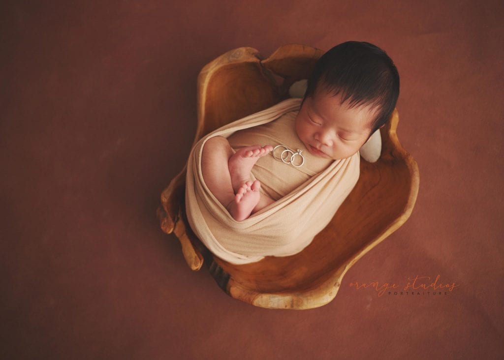 newborn baby in wooden bowl prop with parents' wedding bands and rings in singapore home natural lighting
