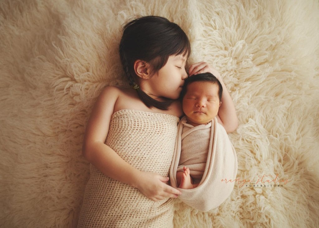 elder sister kissing baby brother newborn portraits in singapore studio