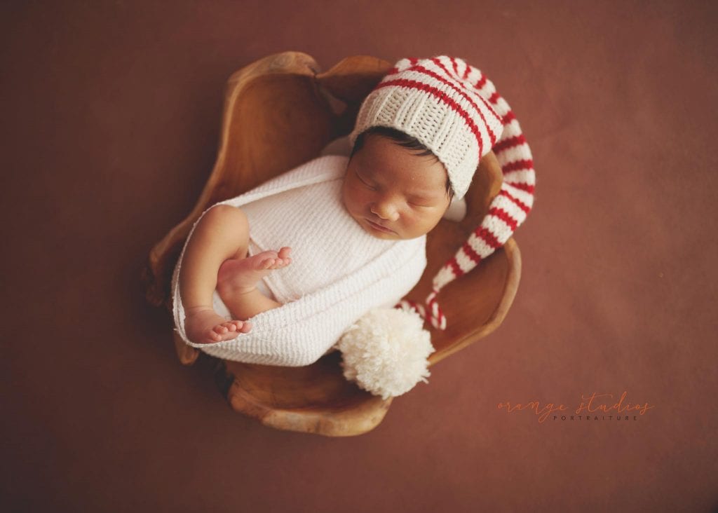 8 days old baby boy wearing christmas hat in wooden bowl newborn portraits in singapore studio