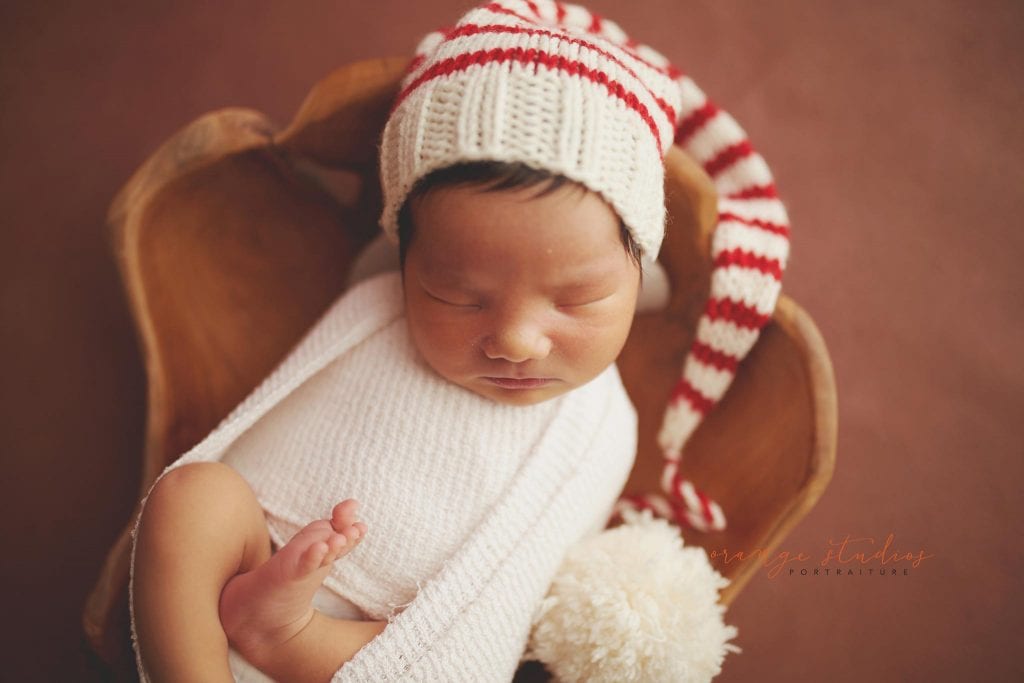 8 days old baby boy wearing christmas hat in wooden bowl newborn portraits in singapore studio