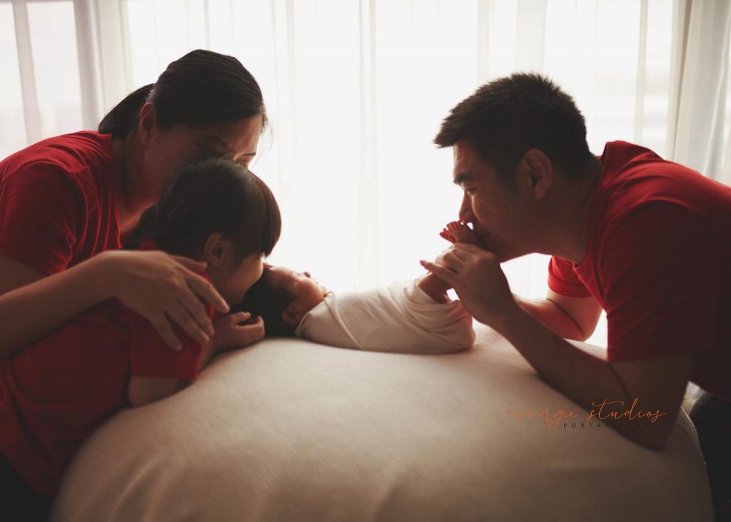 parents and elder sister kissing 8 days old baby boy newborn portraits in singapore studio