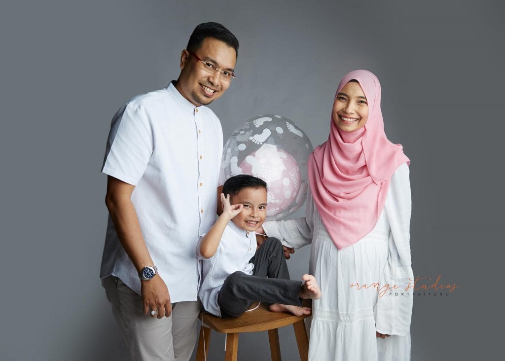malay muslim maternity portraits with family holding gender reveal balloon in singapore studio