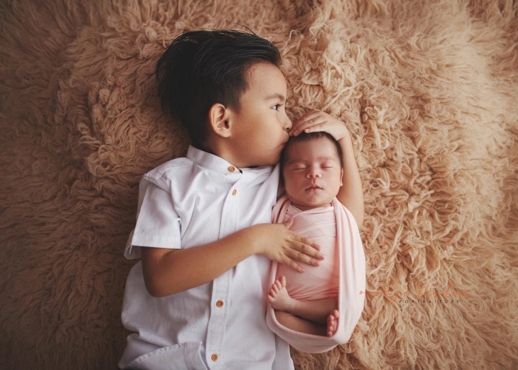 elder brother kissing 7 days old newborn baby sister portraits in singapore studio