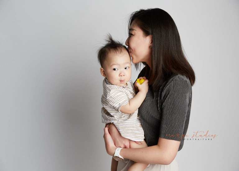 mum kissing 1 year old baby boy family portraits in singapore studio