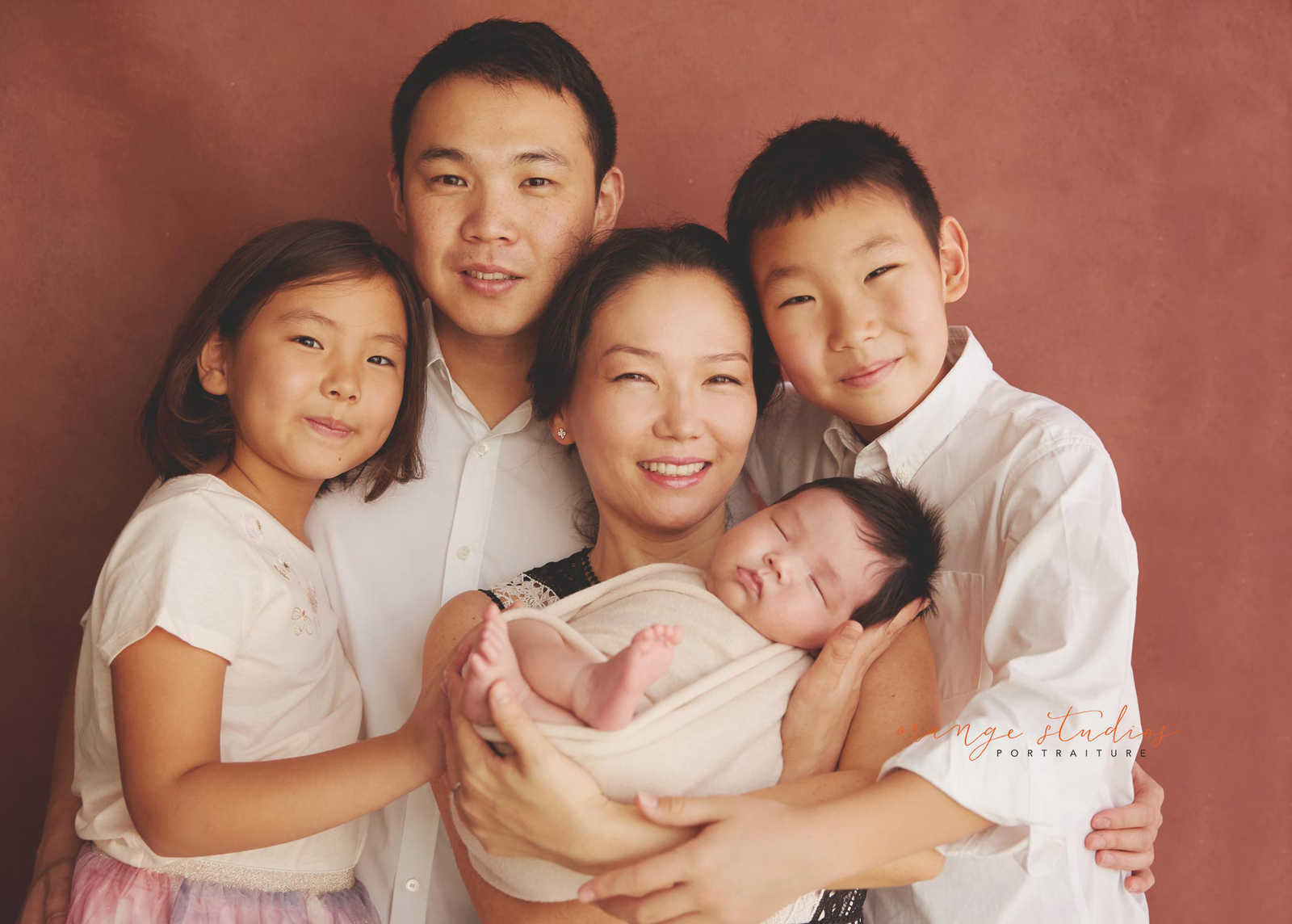 family of five smiling with a newborn looking at the camera